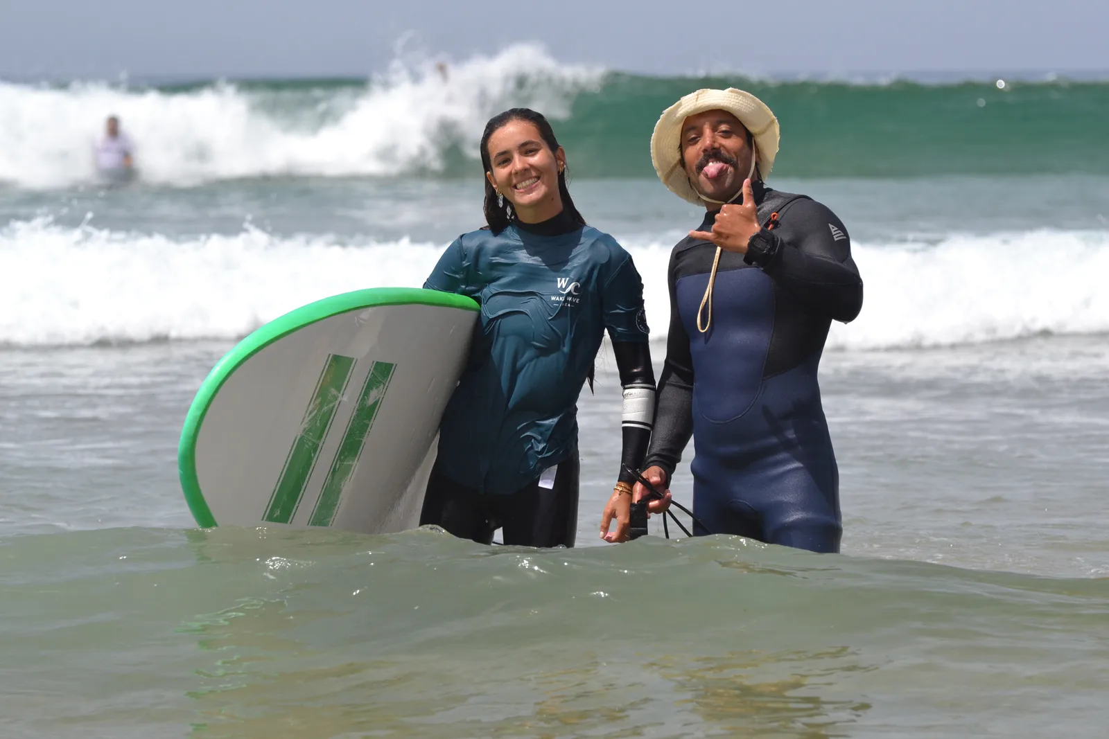 Two people beside a green surfboard in the water during a Wake Wave session.