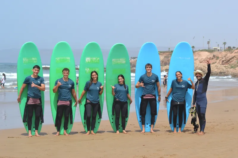 A Wake Wave group standing together on the beach with green and blue surfboards.